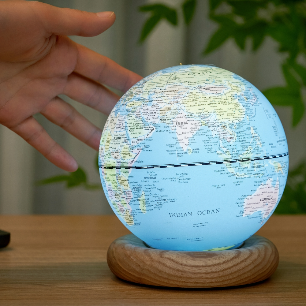 Gingko Mini Light Blue Atlas Globe with White Ash Base lit with a hand